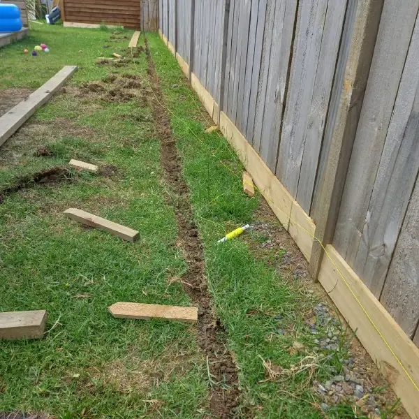 The starting point: a shallow trench dug along the fence line in the lawn, string line out and timber offcuts lying on the grass