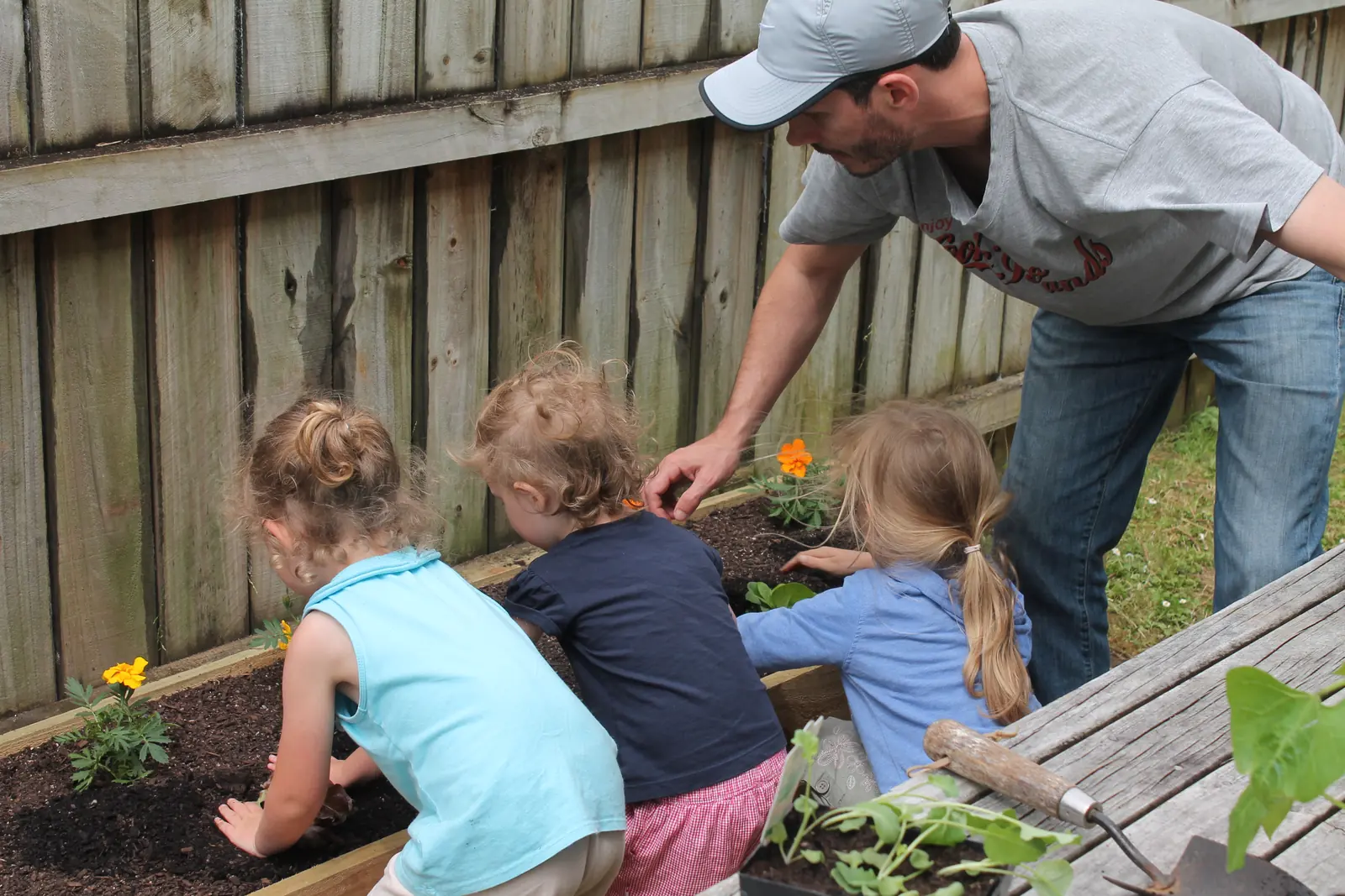Planting marigolds into the raised bed with my three girls, all of us crouched down with our hands in the soil