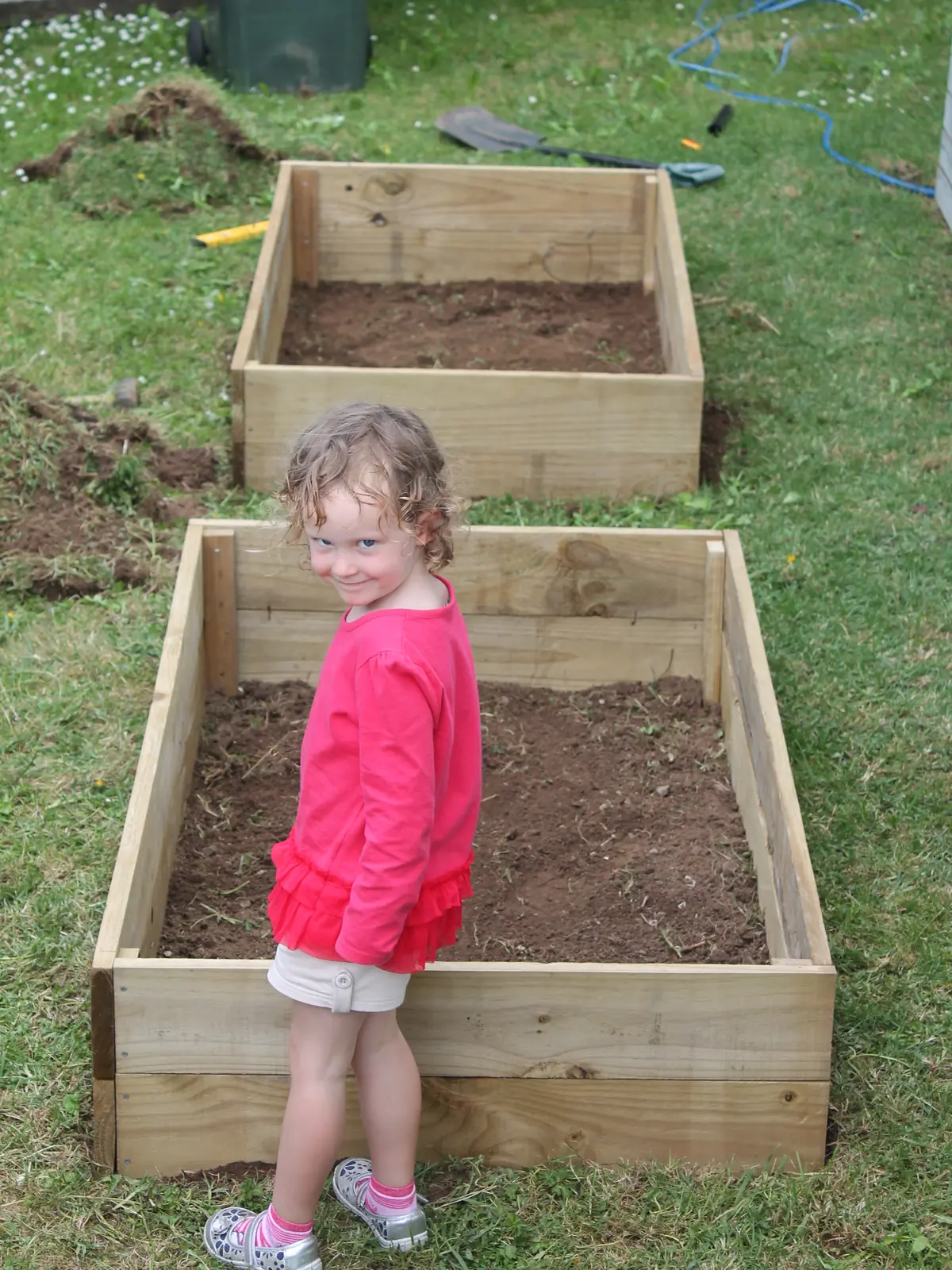 Two newly built raised garden beds cut into the lawn at the rental in 2014, filled with fresh soil, with one of my kids standing beside them