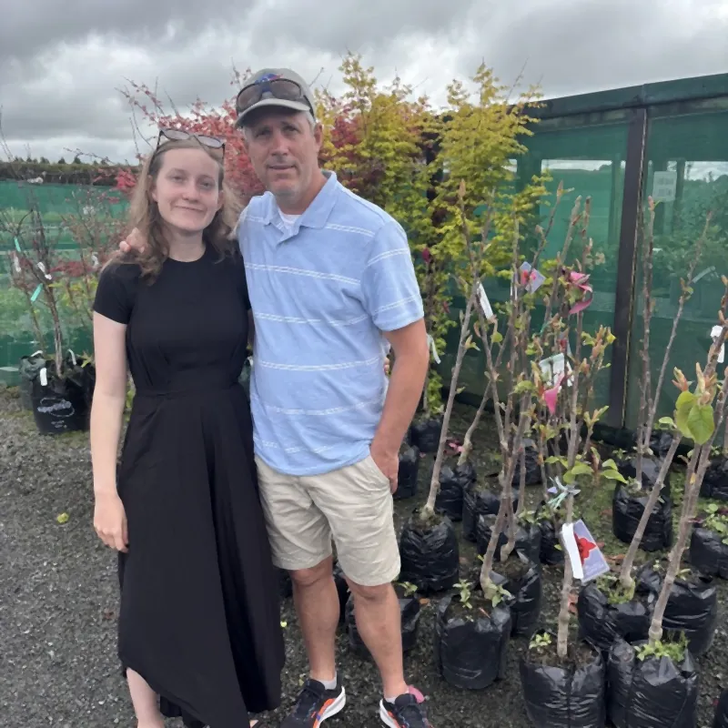 Me and my daughter at the nursery, standing beside rows of young trees in their bags