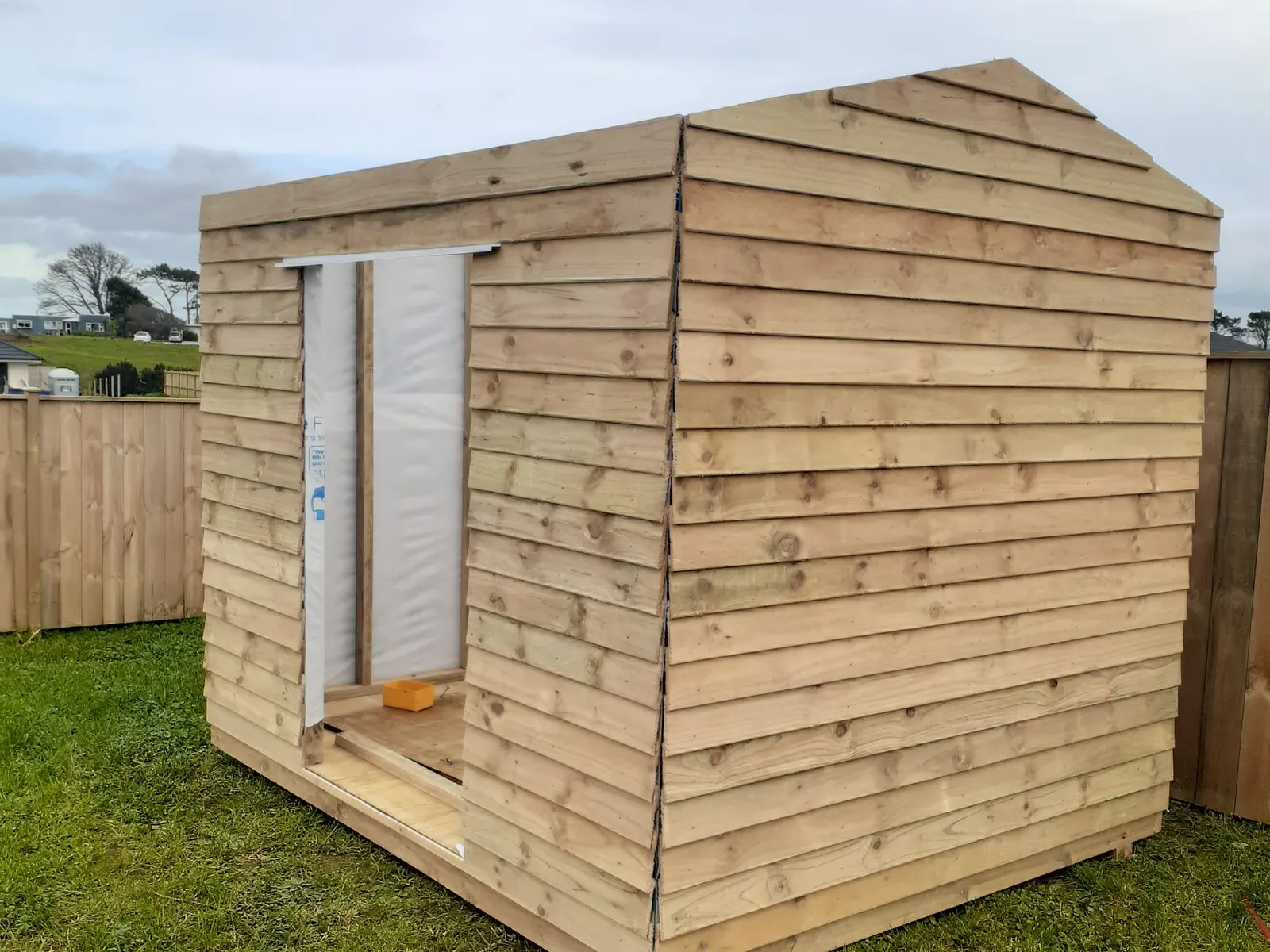 The shed part-built in 2020: bare untreated timber, no doors on yet, standing on open grass