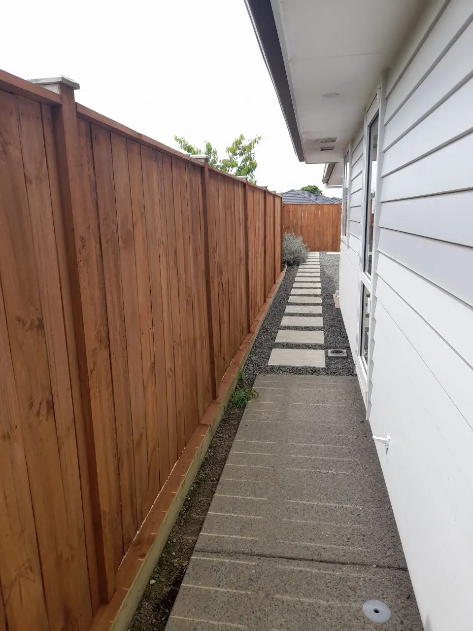 The stained fence running the length of the side path, rich warm brown against the white weatherboards of the house
