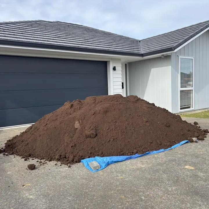 A mountain of soil tipped onto a blue tarp on the driveway in front of the garage