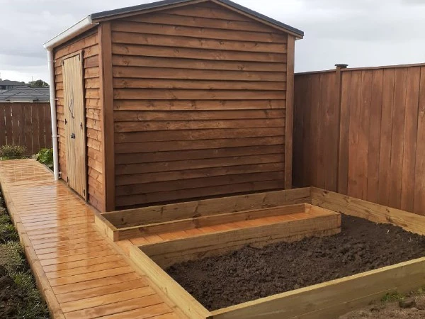 The finished timber walkway running past the stained shed in 2025, with a new raised bed alongside it full of fresh soil